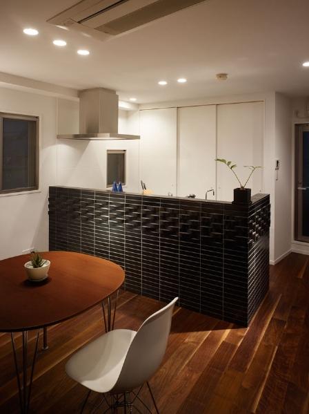 キッチンカウンターは2種類の黒いタイルを張り分け、個性的に演出。背面には大きな収納を設けて収納量を確保しつつ、白で壁と同化させることで、キッチンの明るさやDKにおける黒いカウンターの印象をさらに引き立てている。